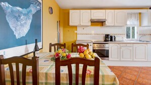 A kitchen with white cabinets, a dining table with a floral tablecloth, and a large map on the wall. - 'Biofinca Las Dulces Casa Almita' with Sea View, Private Terrace and Wi-Fi (Guia de Isora)