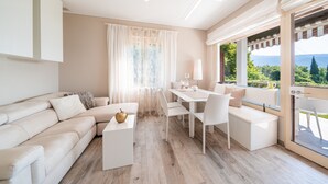 A modern living room with a sofa, dining table, and chairs, a white coffee table, and a view through a glass door. - Apartment 'Wieser Garda Lake' with Lake View, Wi-Fi and Air Conditioning (Gargnano)