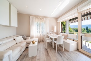 Una sala moderna con sofá, mesa de comedor y sillas, una mesa de centro blanca y vistas a través de un ventanal.