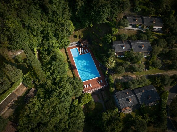 Vista aérea de una zona residencial con piscina, rodeada de abundante vegetación y casas con tejados inclinados.