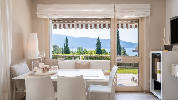 A modern room with a dining area, a sofa, a TV, and a view of mountains and greenery. - Apartment 'Wieser Garda Lake' with Lake View, Wi-Fi and Air Conditioning (Gargnano)