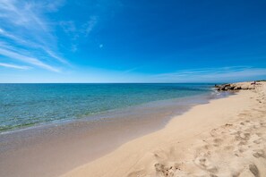A beach with clear blue water, sandy shore, and rocky outcrops.