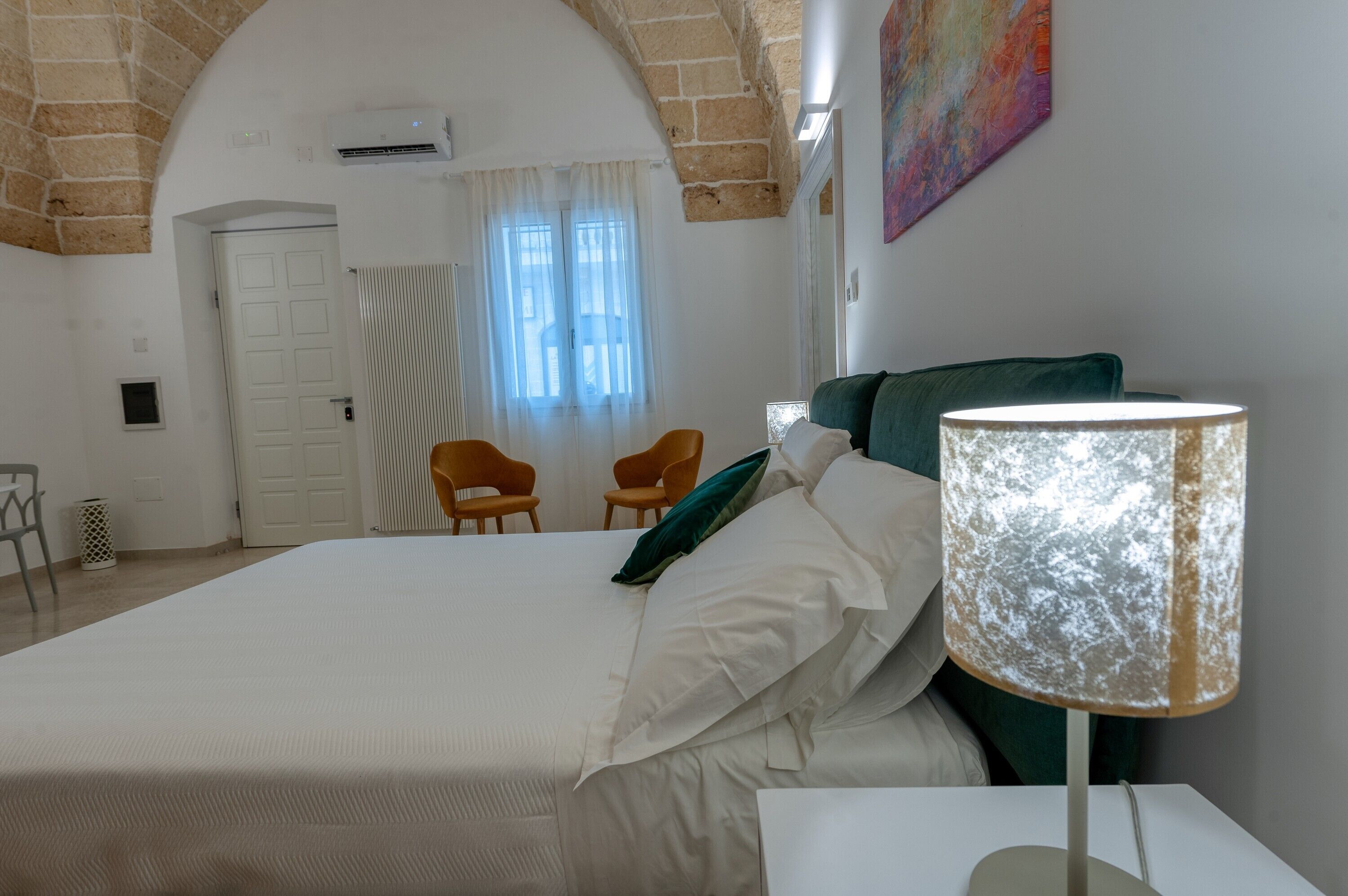 Un dormitorio con una cama grande, dos sillas, una lámpara y una puerta.
