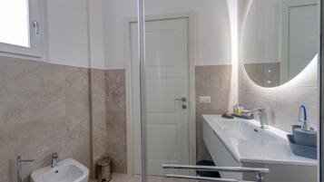 Une salle de bain moderne avec une douche à parois de verre, un lavabo blanc doté d’un robinet bleu et un miroir à cadre incurvé.