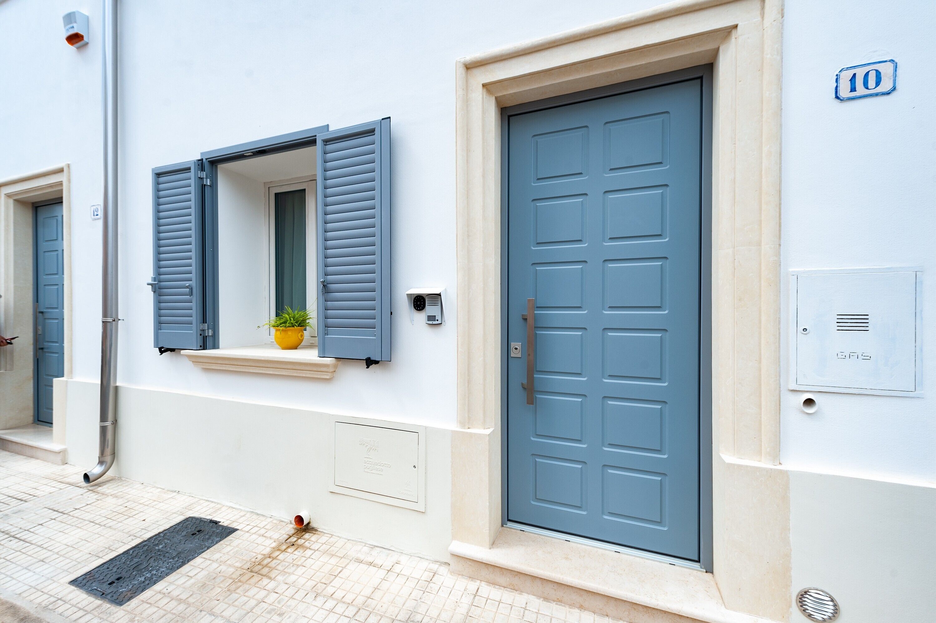 Un bâtiment avec une porte bleue, une fenêtre avec des volets et une petite plante sur le rebord de la fenêtre.