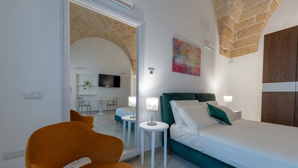 A bedroom with a bed, a chair, a small table, a TV, and a stone ceiling.