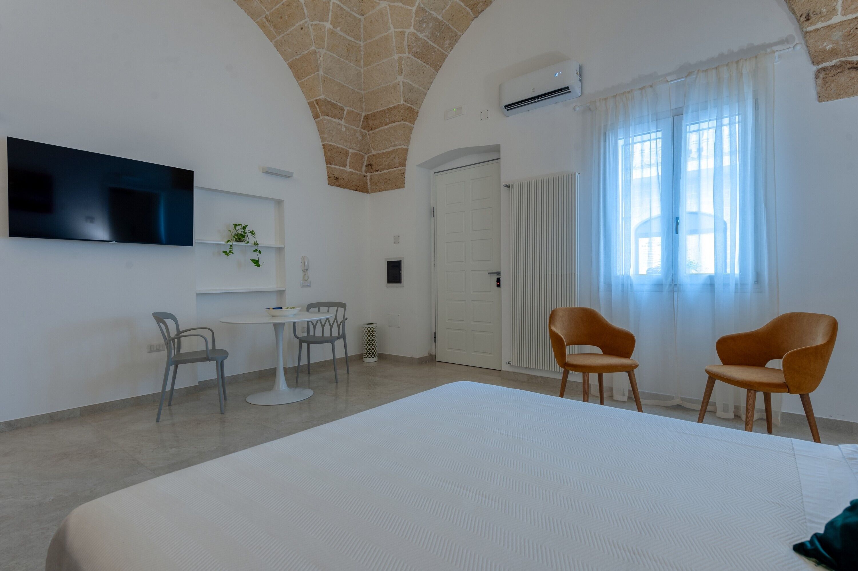 Une chambre d’hôtel avec un grand lit, un téléviseur fixé au mur, une petite table avec deux chaises et une fenêtre avec des rideaux.
