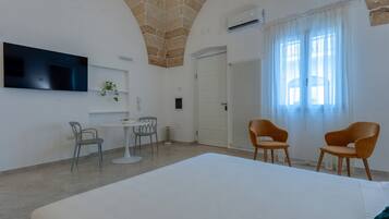 Une chambre d’hôtel avec un grand lit, un téléviseur fixé au mur, une petite table avec deux chaises et une fenêtre avec des rideaux.