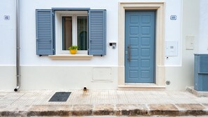 A building with a blue door, a window with blue shutters, and a number plaque.