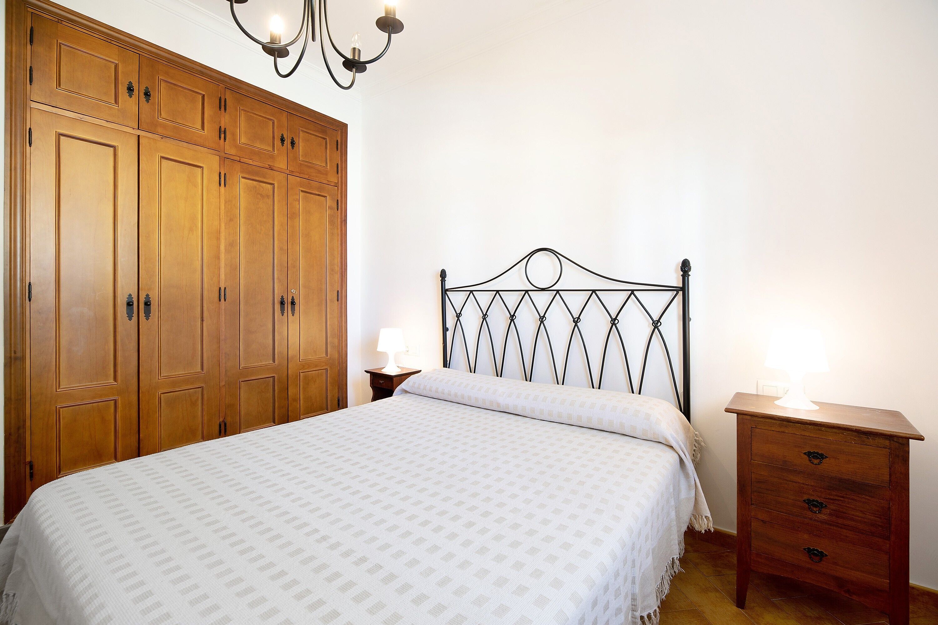 Una camera da letto con un letto, un'armadio in legno, un comodino e un lampadario.