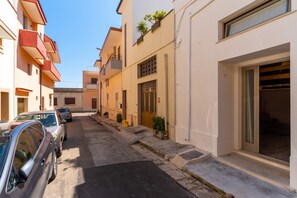 Une rue étroite bordée de voitures garées, des immeubles dotés de balcons et un ciel dégagé.