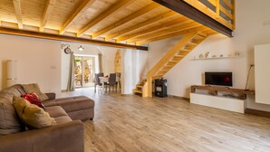 A spacious living area with a high ceiling, wooden beams, a sofa, a TV on a wooden stand, and a staircase leading to an upper level. - Apartment 'Casa Incanto' with Private Garden and Air Conditioning (Presicce-Acquarica)