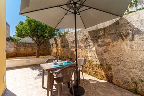 Une terrasse extérieure avec une table et des chaises, un grand parasol et un mur en pierre.