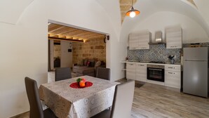 A dining area with a table set for two, a kitchen with modern appliances, and a stone wall. - Apartment 'Casa Incanto' with Private Garden and Air Conditioning (Presicce-Acquarica)