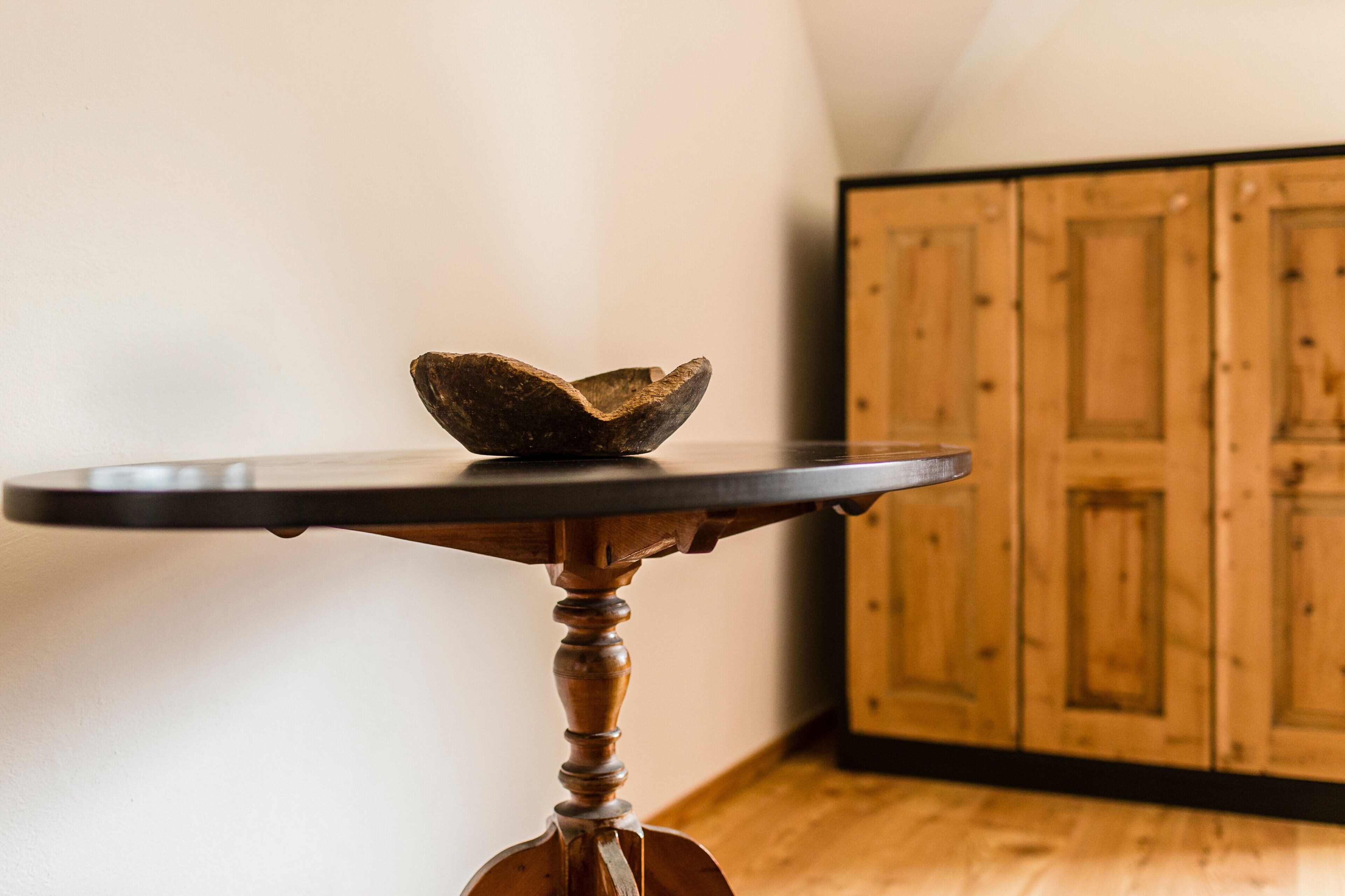 Une table ronde en bois, dotée d’un plateau foncé et surmontée d’un bol, est placée dans une pièce dont l’arrière-plan est constitué de meubles en bois.