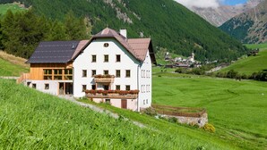 Un edificio blanco con techo inclinado, un balcón lleno de flores y vistas a un valle verde y montañas.