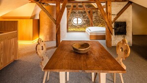 A rustic wooden dining table with chairs, a stone wall with a circular window, and a bed in the background. - Studio Apartment "Josephus Domicilium IV" with Mountain View, Shared Terrace & Wi-Fi (Madonna di Senales)