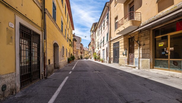 Una calle estrecha flanqueada por edificios, con el número 29 visible en un edificio a la izquierda y una tienda con un letrero a la derecha.
