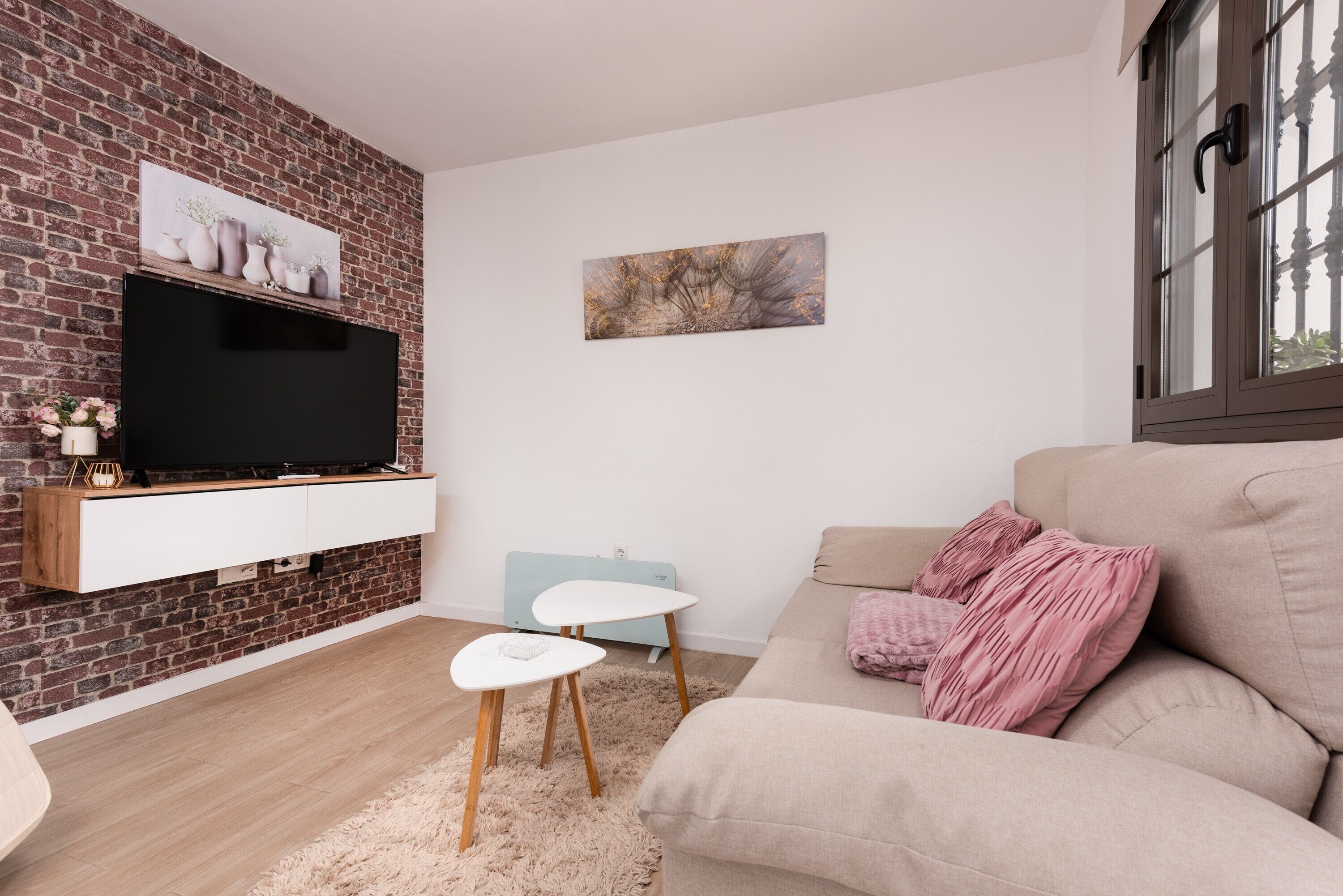 Ett modernt vardagsrum med en tegelvägg, en platt-TV, en ljusblå fåtölj, en beige soffa och en mjuk matta.