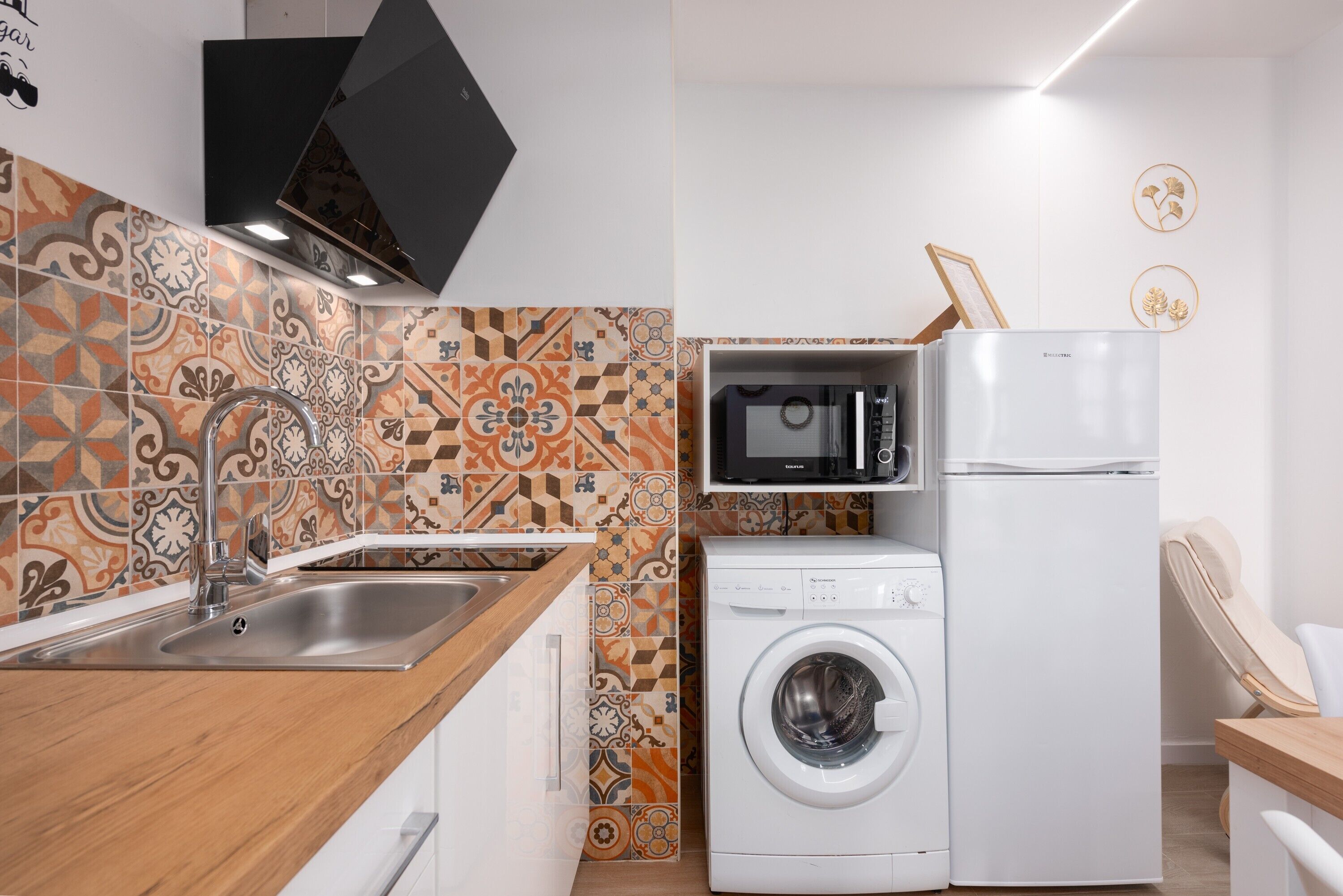 Una cocina compacta con lavadora, microondas y pileta.