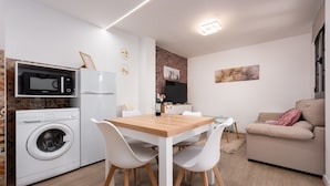A compact living space with a washing machine, microwave, refrigerator, dining table, and a sofa.