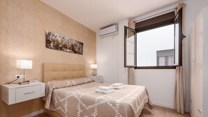 A bedroom with a bed, bedside tables, an air conditioning unit, a window with curtains, and a wall-mounted artwork.