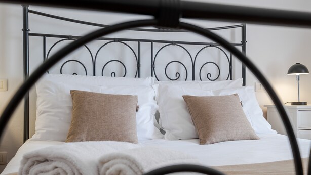 A neatly made bed with white and beige pillows, a metal headboard, and a rolled white towel on the bed. - 5 minutes from Lake Garda, Dimora "Charme of Butterfly (Cavaion Veronese)