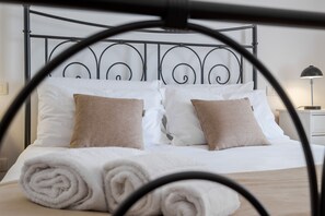 Een net opgemaakt bed met witte en beige kussens, een metalen hoofdbord en een opgerolde witte handdoek op het bed.