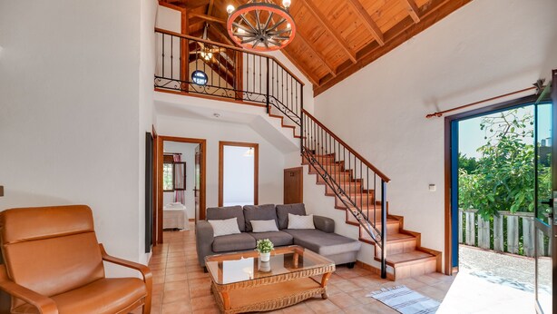 Un vaste espace de vie comprenant un canapé, un fauteuil, une table basse et un escalier menant à un niveau supérieur.