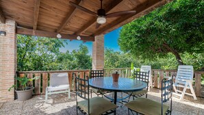 Une terrasse extérieure avec une table ronde et des chaises, entourée d’une clôture en bois et de plantes en pot.