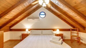 Une chambre avec un plafond en pente, un lit recouvert d’une couvre-lit à rayures, deux tables de chevet avec des lampes, une échelle en bois et un appareil de climatisation.