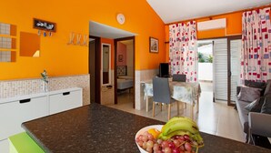 A kitchen with a fruit bowl, a dining area with a table and chairs, and a living area with a sofa. - Vacation Home 'Haus Brigitte' with Shared Pool, Wi-Fi and Air Conditioning (Playa del Inglés)