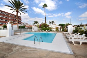 Une piscine entourée de chaises longues, de palmiers et, au fond, un bâtiment d’hôtel.