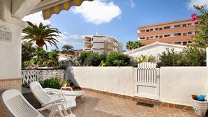 A patio with white lounge chairs, a white wall with a gate, and a building in the background. - Vacation Home 'Haus Brigitte' with Shared Pool, Wi-Fi and Air Conditioning (Playa del Inglés)
