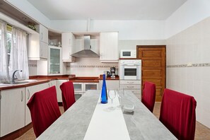A compact kitchen with white cabinets, a microwave, a stove, and a dining table with red chairs.