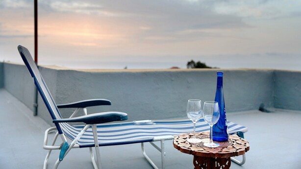 A lounge chair and table with two glasses and a blue bottle on a balcony with a view. - Chalet "Casa Barreto" with Sea View, 3 Private Terraces & Wi-Fi (Puerto de la Cruz)