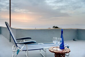 Silla de descanso y mesita con dos vasos y una botella azul en un balcón con vistas.