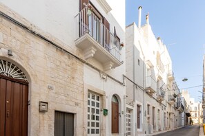Une rue étroite bordée de bâtiments blancs, agrémentée de balcons, de portes en arc de cercle et surplombée d’un ciel d’un bleu éclatant.