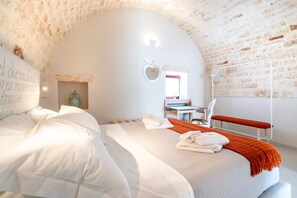 A bedroom with a white bed, a bench, a desk, and a mirror.