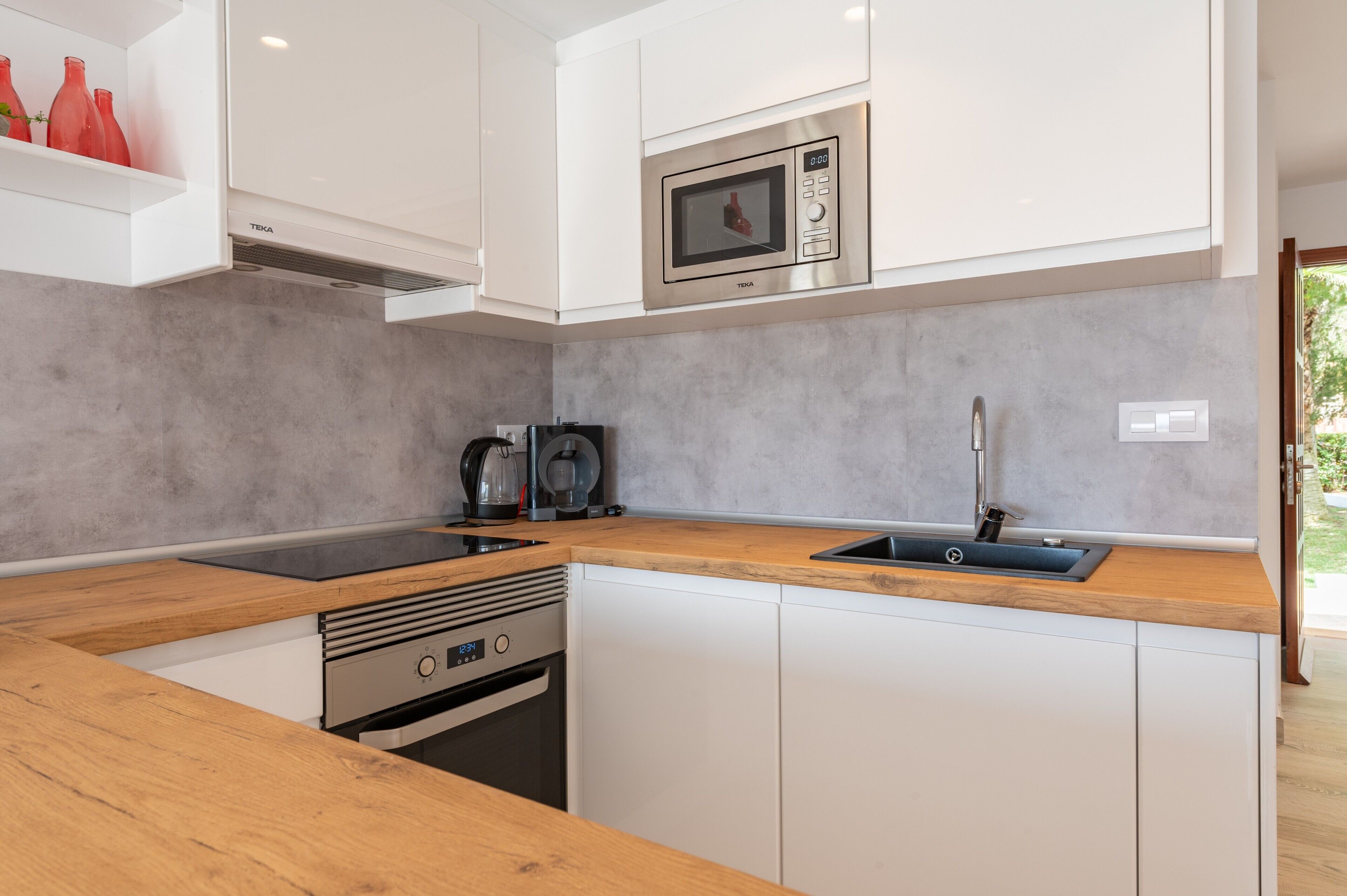 Una cocina moderna con armarios blancos, un microondas de acero inoxidable, horno empotrado y encimera de madera.
