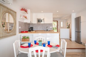 Une cuisine moderne avec des meubles blancs, un four à micro-ondes et un réfrigérateur. On y trouve une table à manger avec des chaises et un set de table rouge.