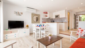 Una sala de estar moderna con televisor de pantalla plana, comedor con sillas, cocina con armarios blancos y un ventanal grande.
