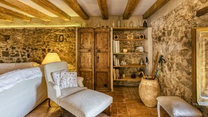 A rustic room with a stone wall, wooden beams, a white sofa, a wooden cabinet, and a bookshelf.