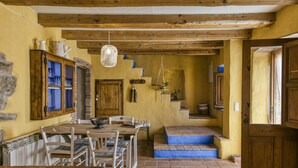 A rustic dining area with a wooden table and chairs, a hanging light fixture, and a staircase leading to an upper level.