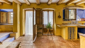A rustic interior with exposed wooden beams, a stone staircase, a small potted plant, and a kitchen area with a sink and tiled backsplash.