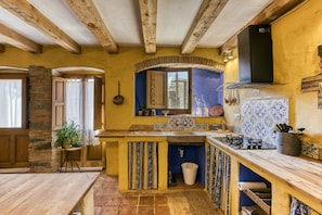 A rustic kitchen with exposed wooden beams, a stone wall, and a blue tiled backsplash. - Holiday Home 'Casa De Pueblo' with Mountain View, Private Terrace and Wi-Fi (CANTALLOPS)