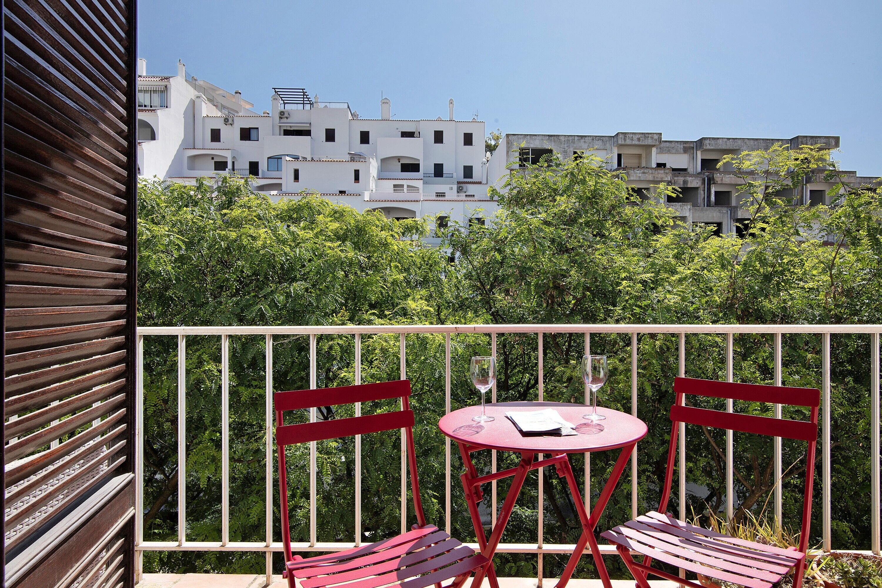 A balcony with red furniture, a clear view of buildings, and a white railing.