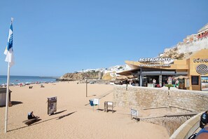 A beachside restaurant with a stone wall, a flag, and a clear view of the beach and ocean.