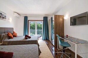 Une chambre d’hôtel avec deux lits, un bureau, une chaise, une télévision et une vue sur la verdure par les fenêtres.
