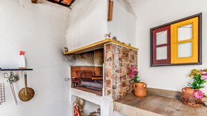 A rustic kitchen with a brick oven, a wooden shelf with kitchen utensils, and a window with a yellow frame. - Holiday Home "O Mundo Da Lua - Galinheiro" with Shared Garden and Wi-Fi (São Simão)